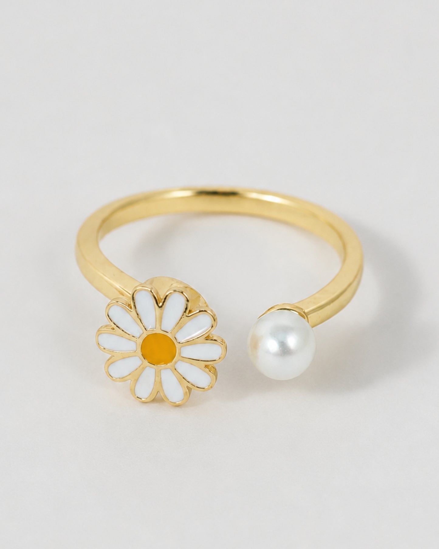 Gold ring with a daisy flower and pearl on a light gray background