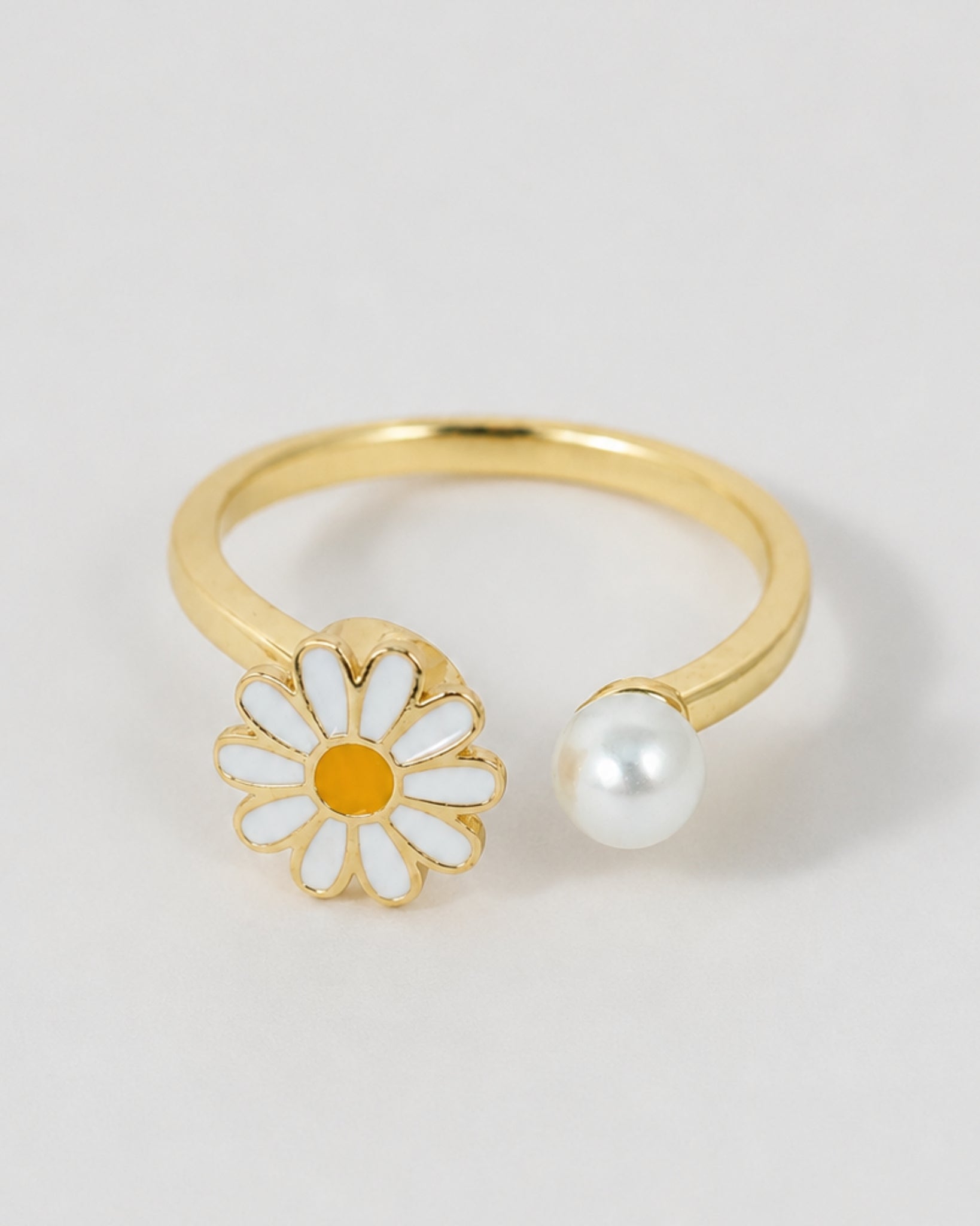 Gold ring with a daisy flower and pearl on a light gray background